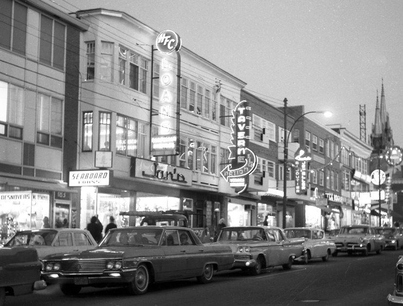 La rue Principale dans les années 1960, alors qu’au déclin du jour, le centre-ville vibrait au rythme des enseignes lumineuses ornant les édifices commerciaux. ( © Société d’histoire de la Haute-Yamaska, fonds Jean-Paul Matton, P42,S39,D1,P16)